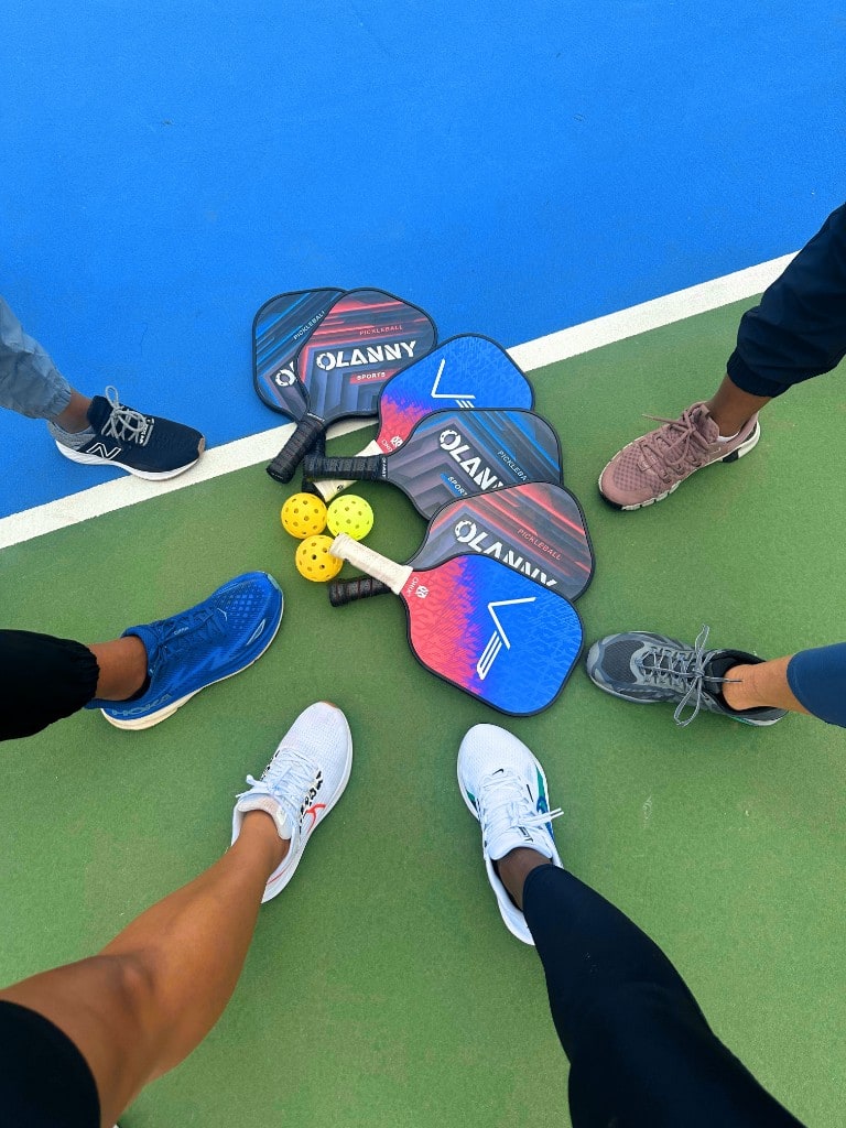 Players gathered in a circle around paddles and balls on court