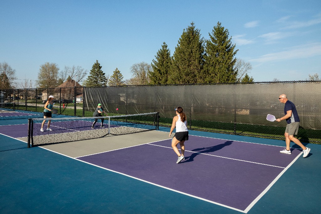 Four players in a doubles open-play pickleball game on an outdoor court